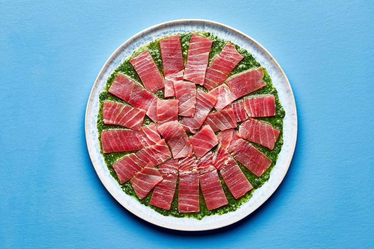 homemade sauce for aguachile spread evenly on a serving platter topped with thinly sliced, raw sushi-grade ahi tuna