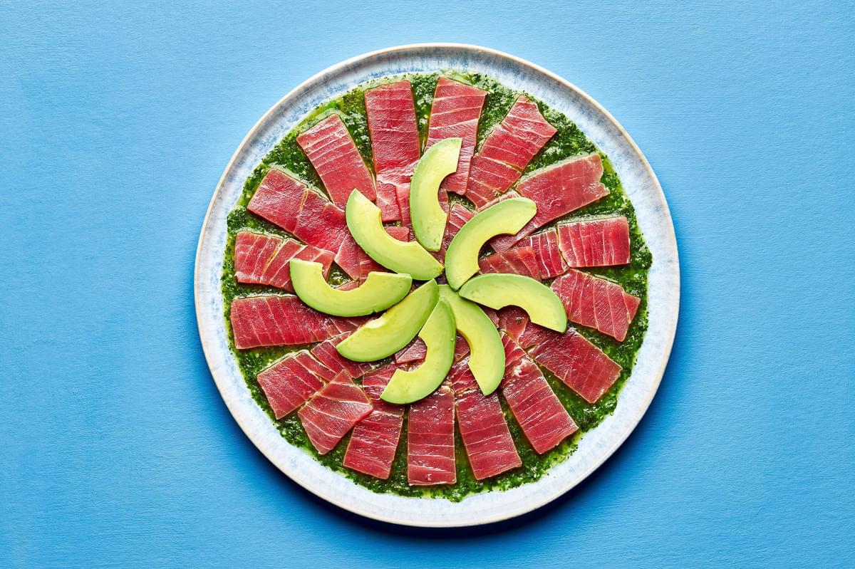 homemade sauce for aguachile spread on a serving platter topped with thinly sliced, ahi tuna and sliced avocado
