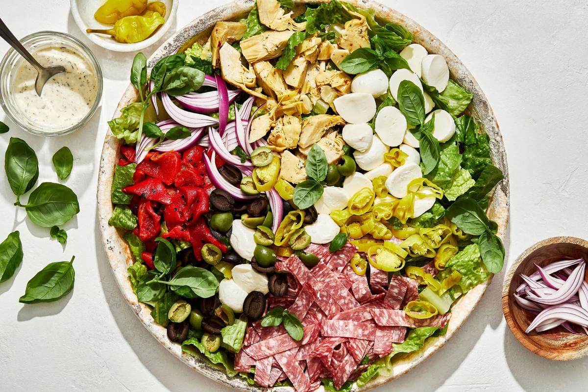 antipasto salad with romaine, salami, mozzarella, basil, and pickled veggies next to a bowl of creamy parmesan lemon dressing