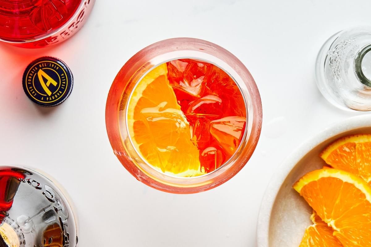 an aperol spritz with prosecco, aperol, and sparkling water and an orange slice to garnish surrounded by the ingredients