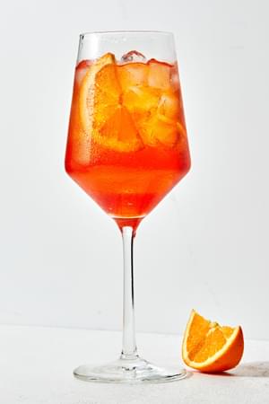 an Aperol Spritz in a stemmed glass over ice with an orange slice as garnish and an orange slice on the counter beside it
