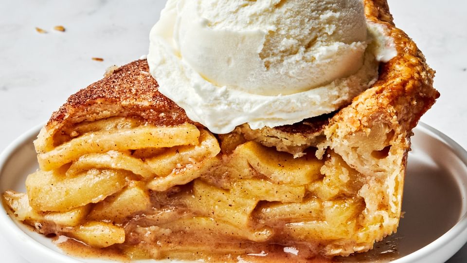 a slice of homemade apple pie topped with vanilla ice cream. Pie is seasoned with brown sugar, cinnamon and nutmeg.