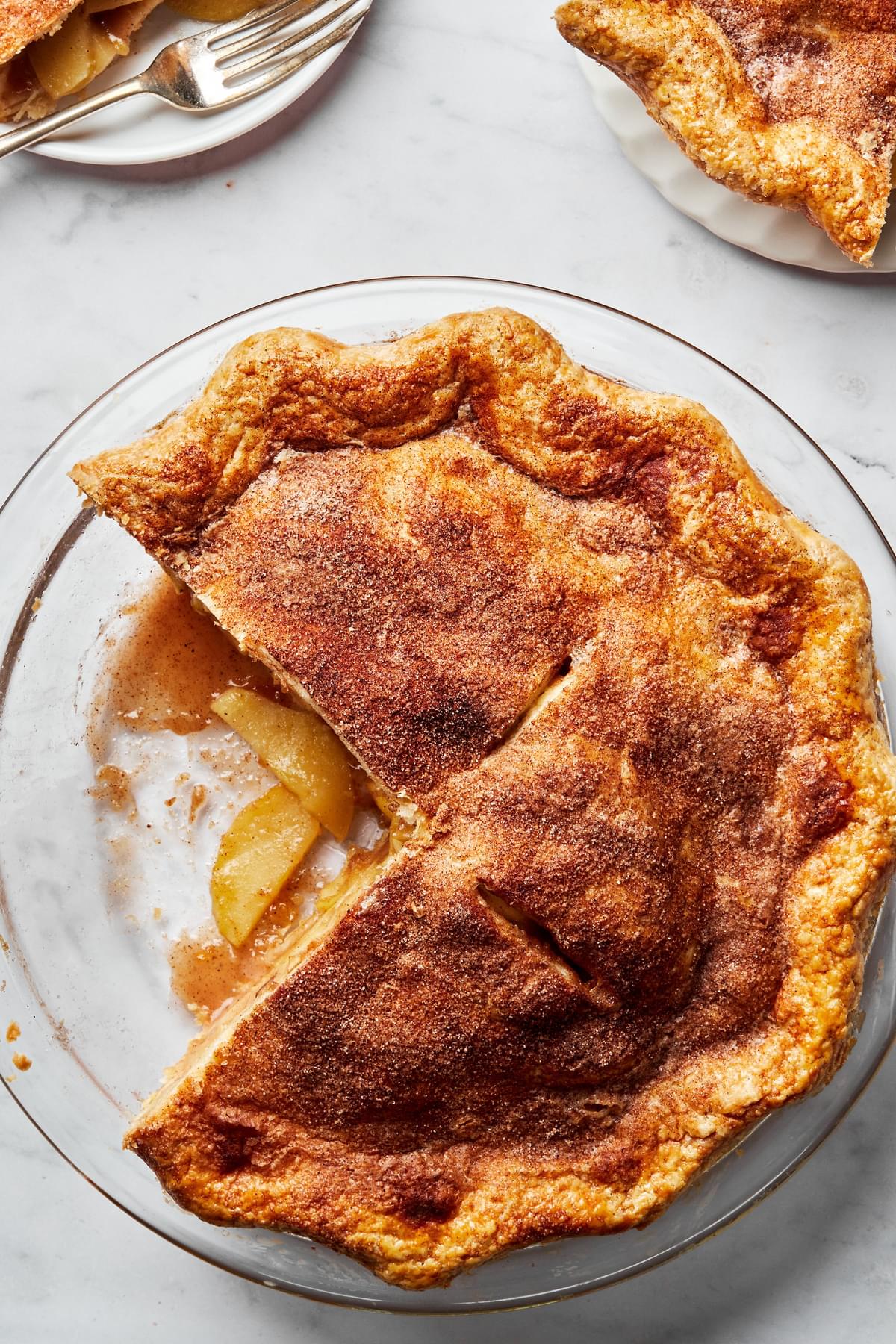 a homemade apple pie with golden crust in a pie pan with a slice that has been cut out