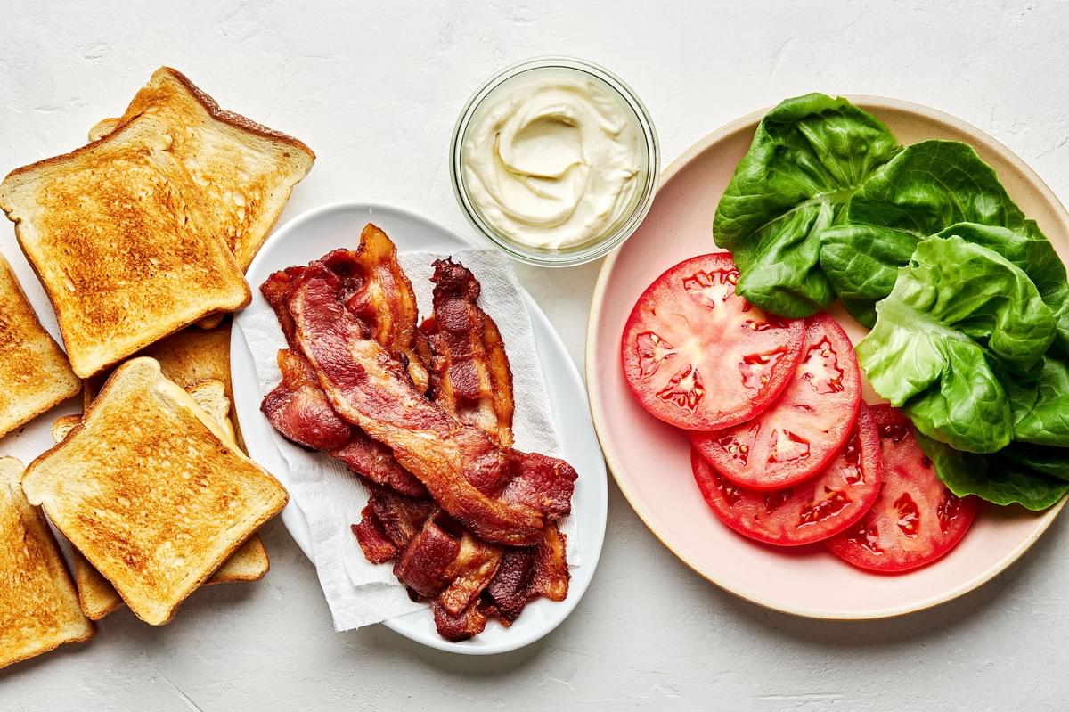 toast, bacon, homemade mayonnaise, sliced tomatoes and lettuce on the counter for making BLTs with homemade mayonnaise