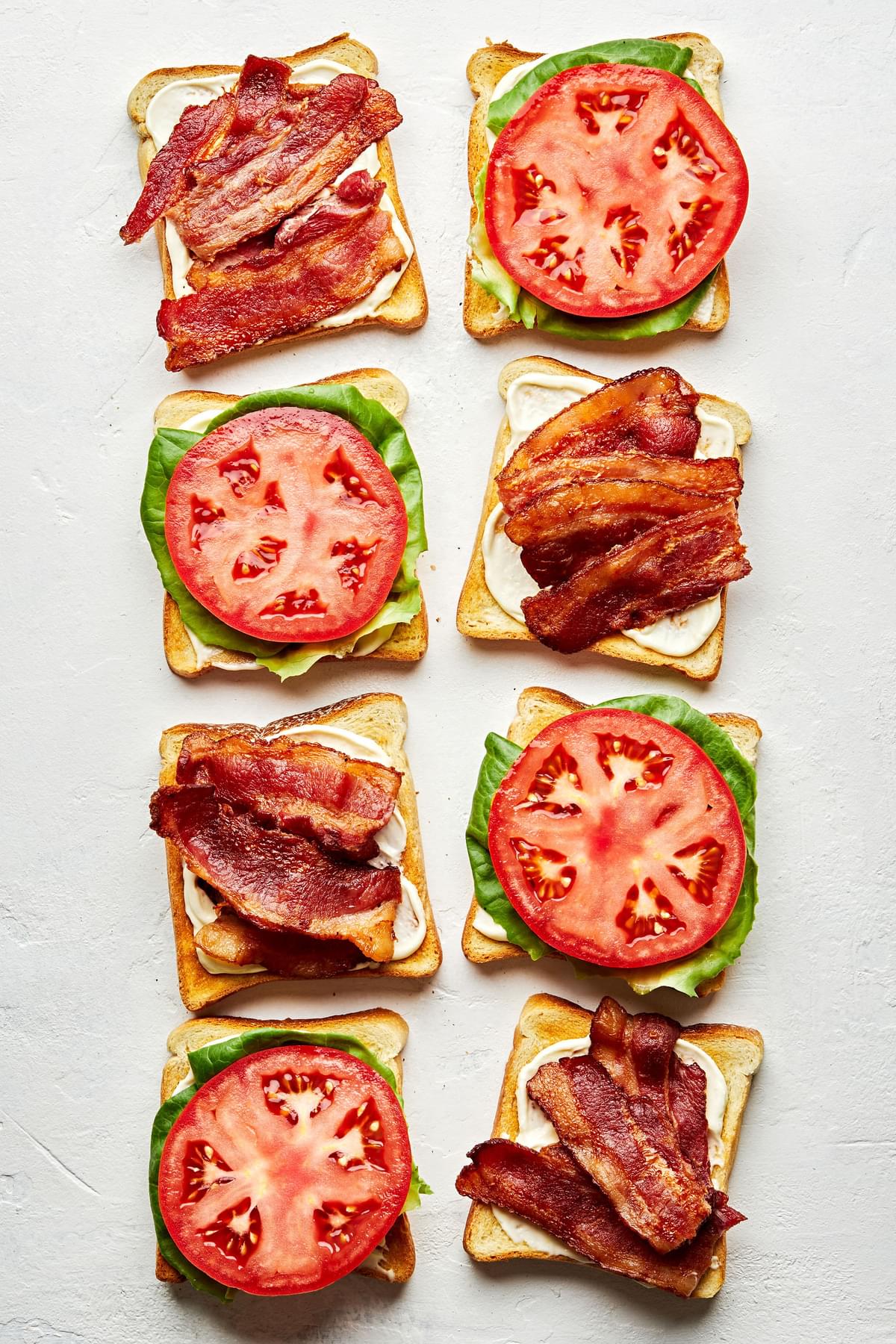 four BLTs being assembled with toast, homemade mayonnaise, bacon, lettuce and sliced tomato