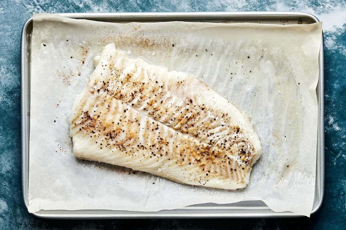 a raw cod filet on a parchment lined baking sheet seasoned with  salt, garlic powder and black pepper