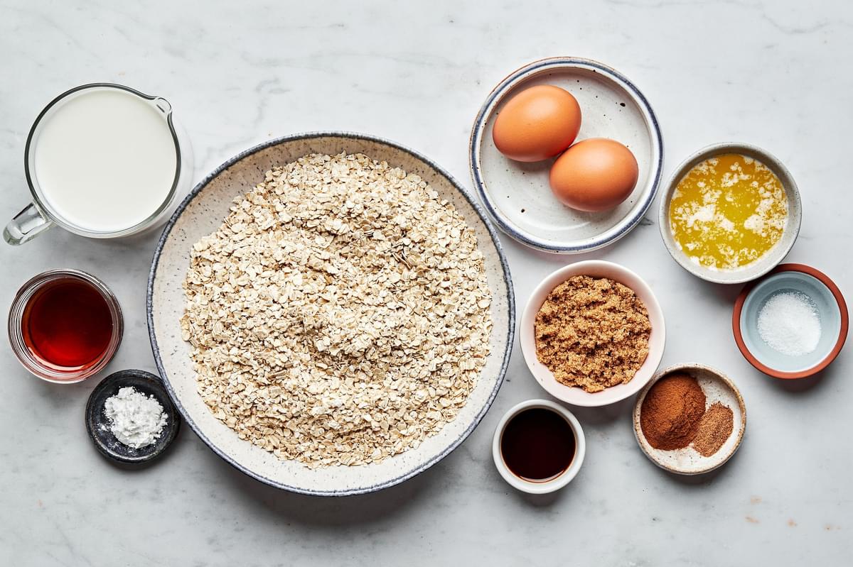 oats, eggs, milk, syrup, vanilla, butter, brown sugar, salt, cinnamon, nutmeg and baking powder in bowls for baked oatmeal
