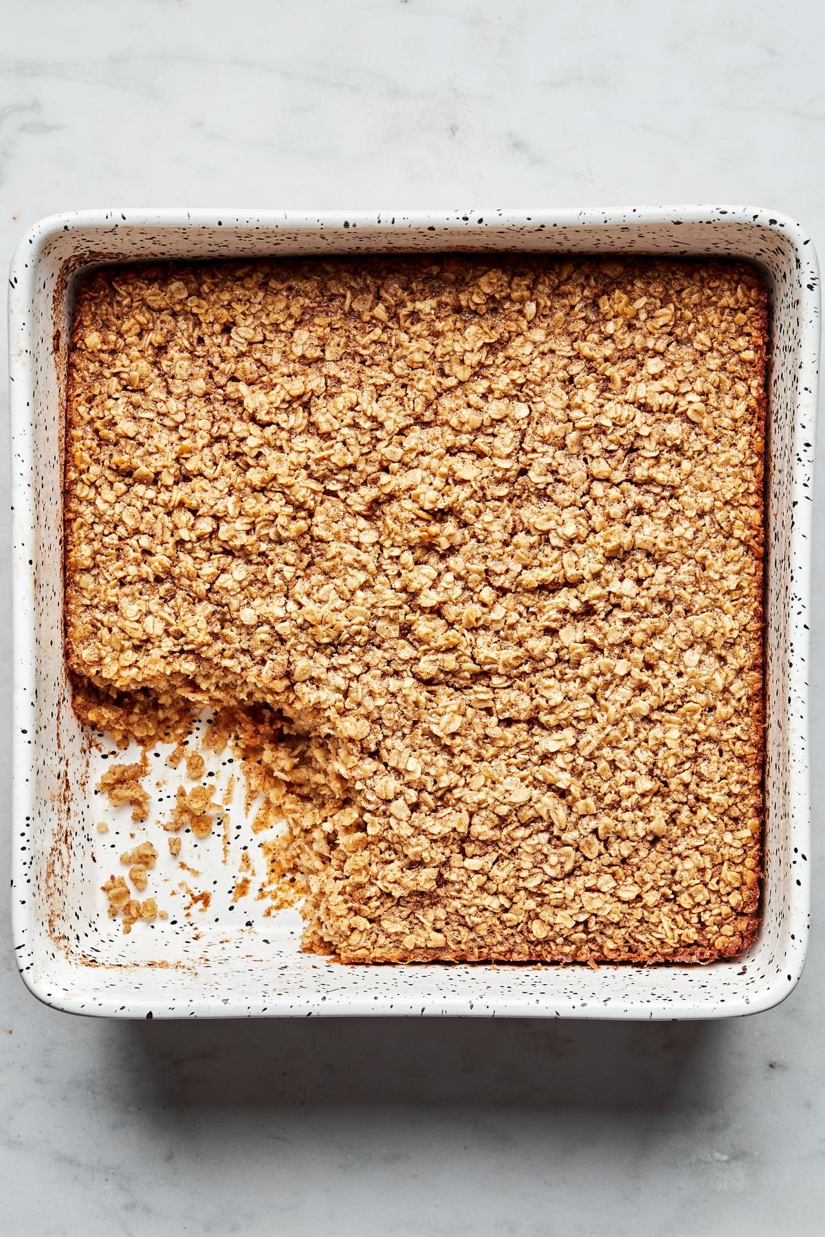 baked oatmeal in a 9x9 baking with a slice cut out, made with oats, eggs, milk, maple syrup, vanilla, butter and spices