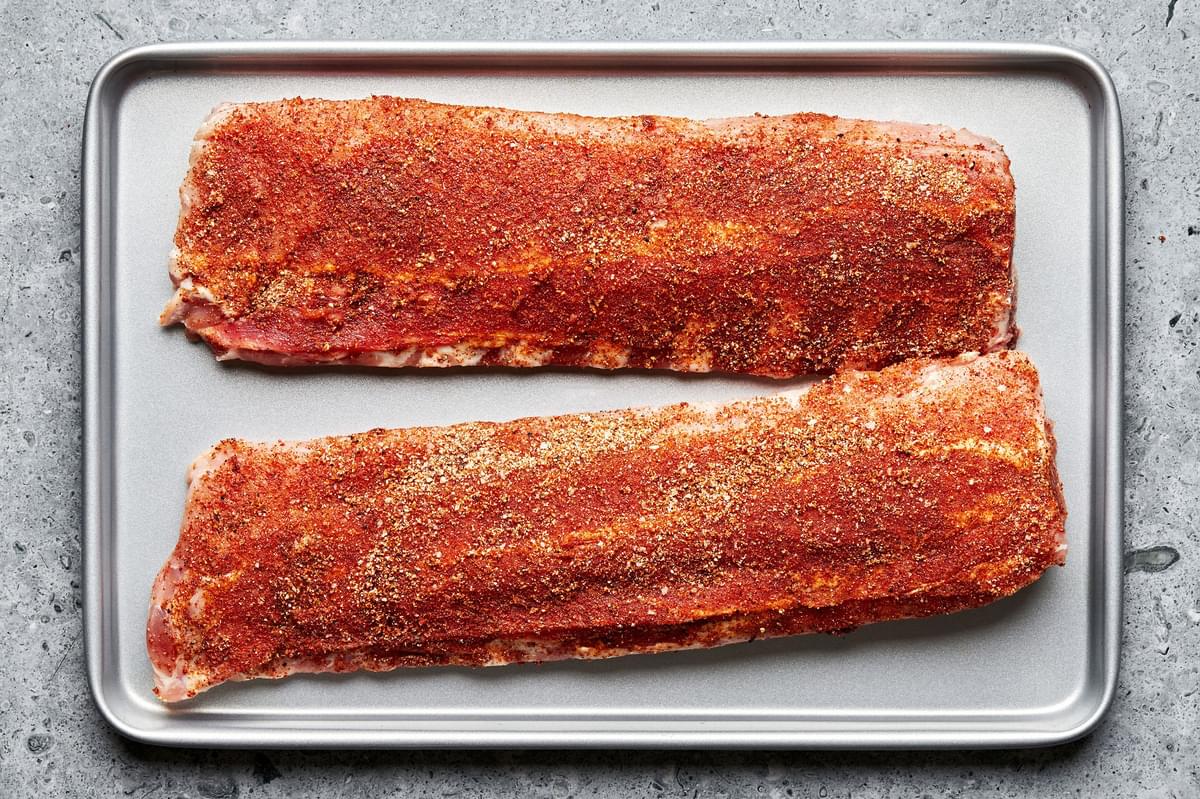 raw pork ribs covered in homemade dry rub on a baking sheet ready to be baked in the oven