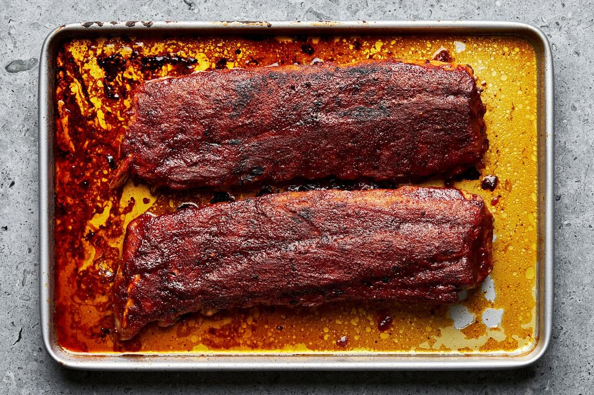 baked pork ribs on a baking sheet that have been slathered with homemade bbq sauce and broiled until caramelized