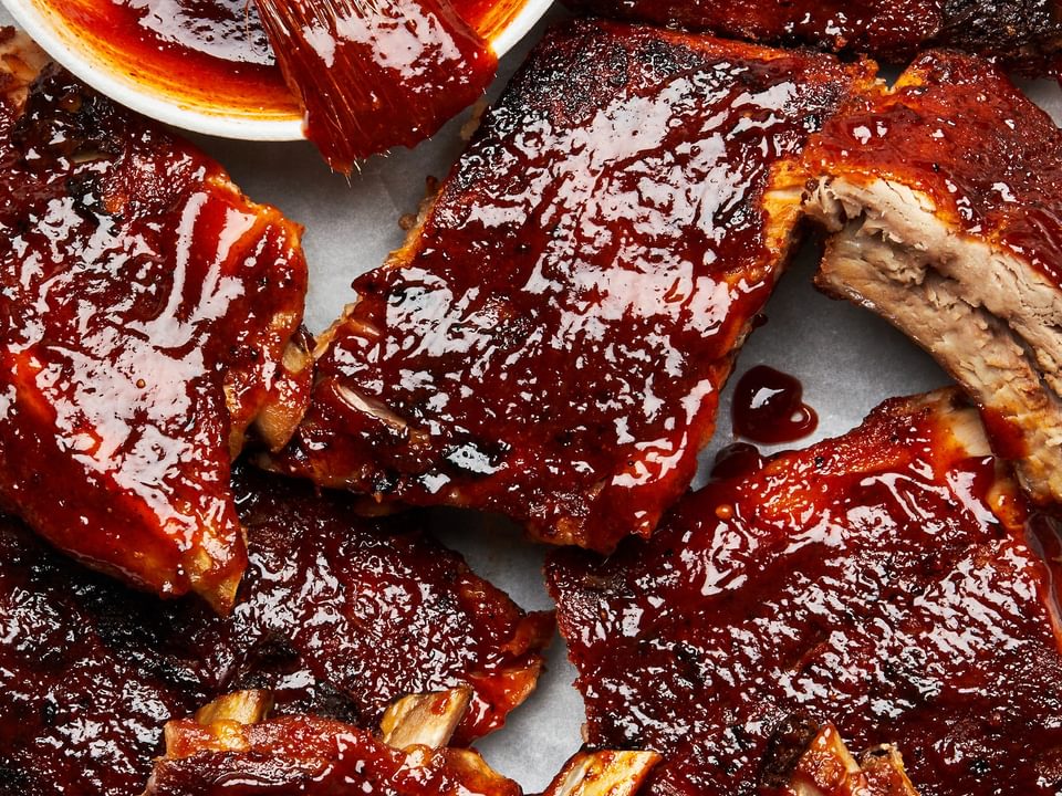 baked pork ribs covered with homemade bbq sauce next to a bowl of extra bbq sauce with a pastry brush