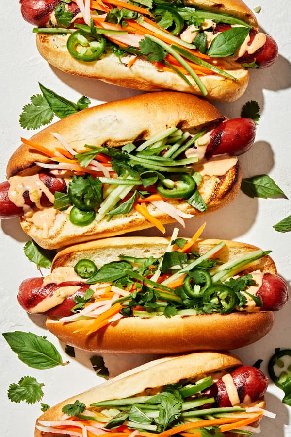 Banh Mi Hot Dogs drizzled with sriracha mayo topped with pickled veggies, cilantro, basil, cucumbers and jalapeños