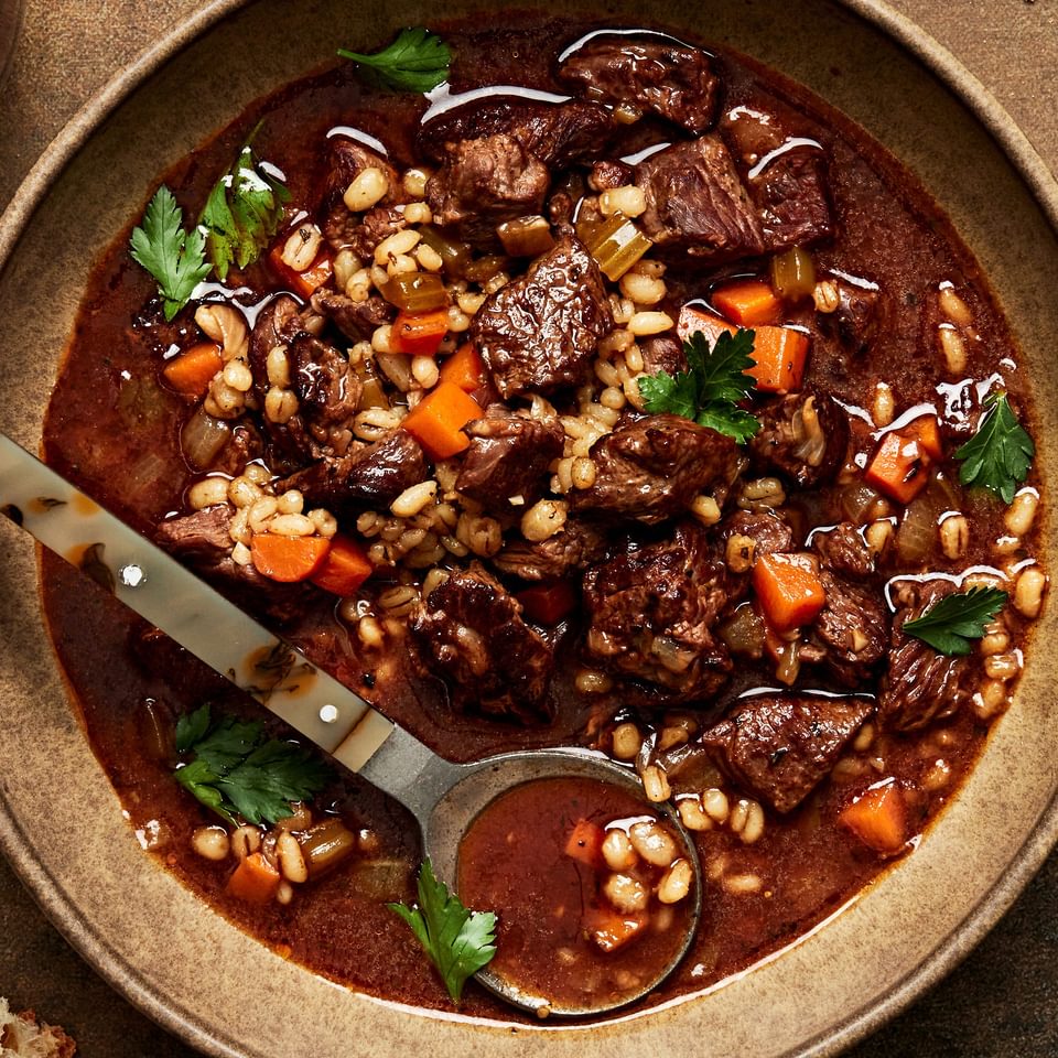 a bowl of homemade Beef & barley soup with spoon made with vegetables, spices, broth, tomato paste and soy sauce