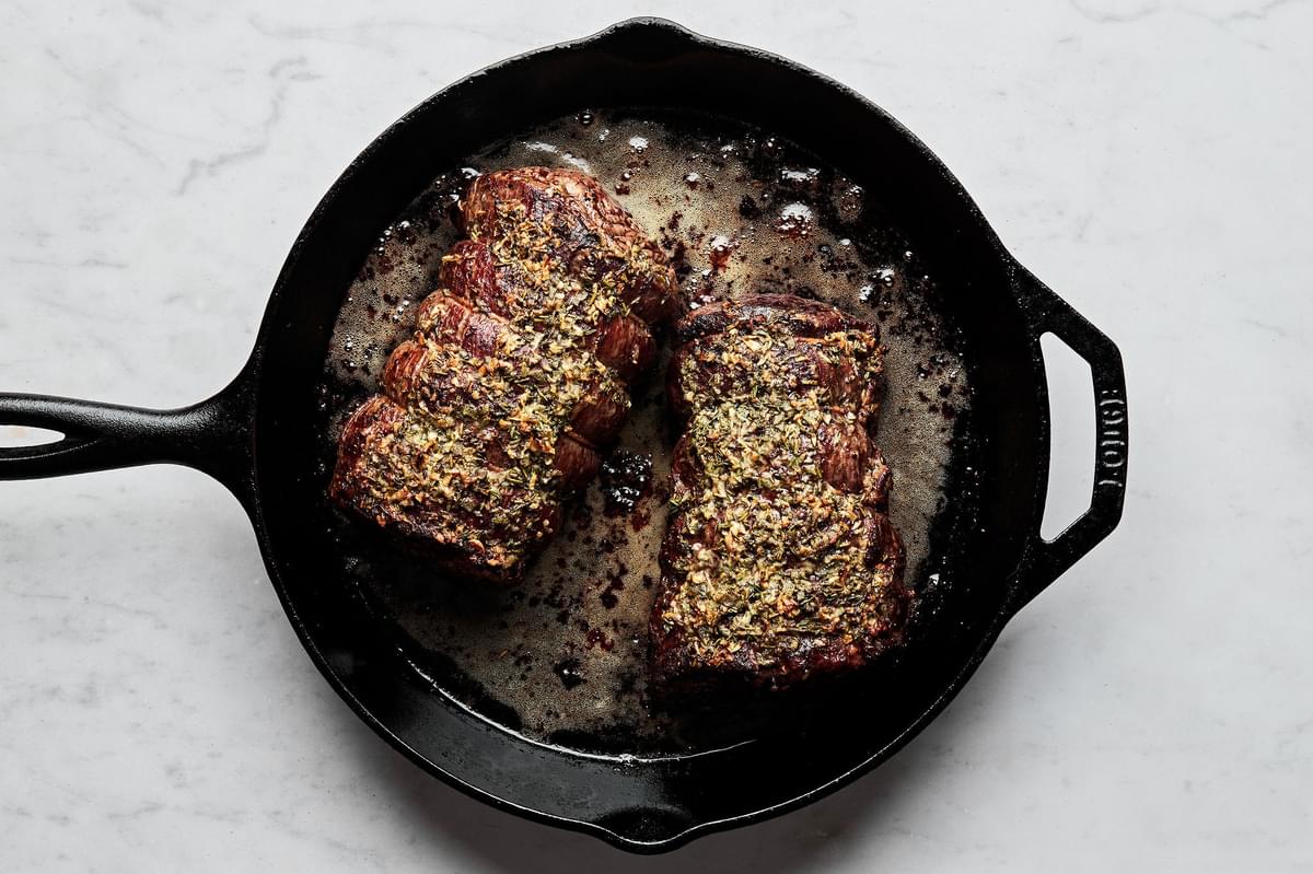 oven roasted beef tenderloin seasoned with salt, pepper and garlic herb butter in a cast iron skillet