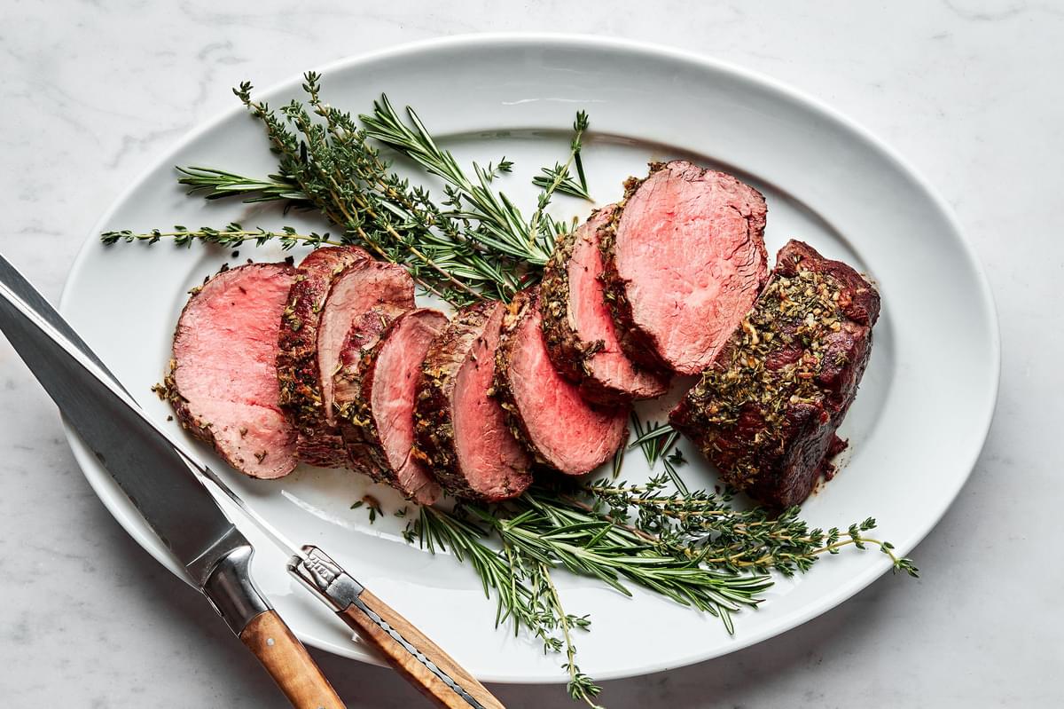 homemade beef tenderloin cooked with garlic herb butter sliced on a serving platter garnished with fresh herbs
