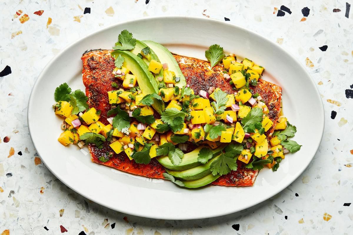 blackened salmon topped with homemade mango salsa and avocado on a serving plate
