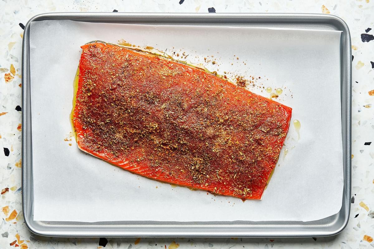 a salmon filet drizzled with olive oil and covered in spice rub on a parchment paper lined baking sheet for blackened salmon
