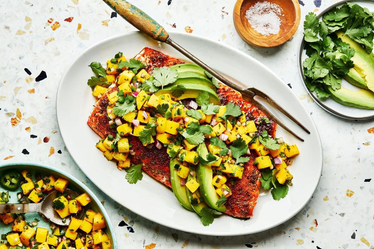 blackened salmon with homemade mango salsa and avocado on a serving plate next to bowls of mango salsa and avocado