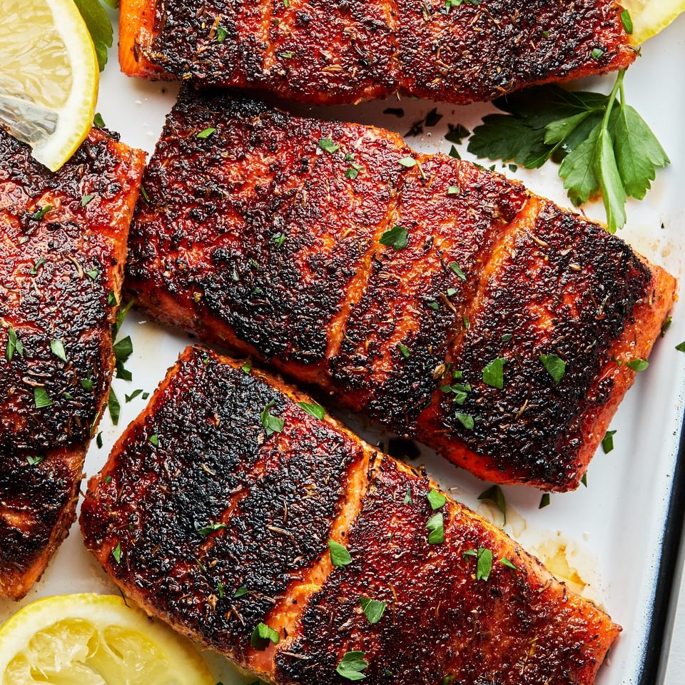 three 4 ounce Blackened salmon fillets on a serving platter with lemon wedges and sprinkled with fresh parsley