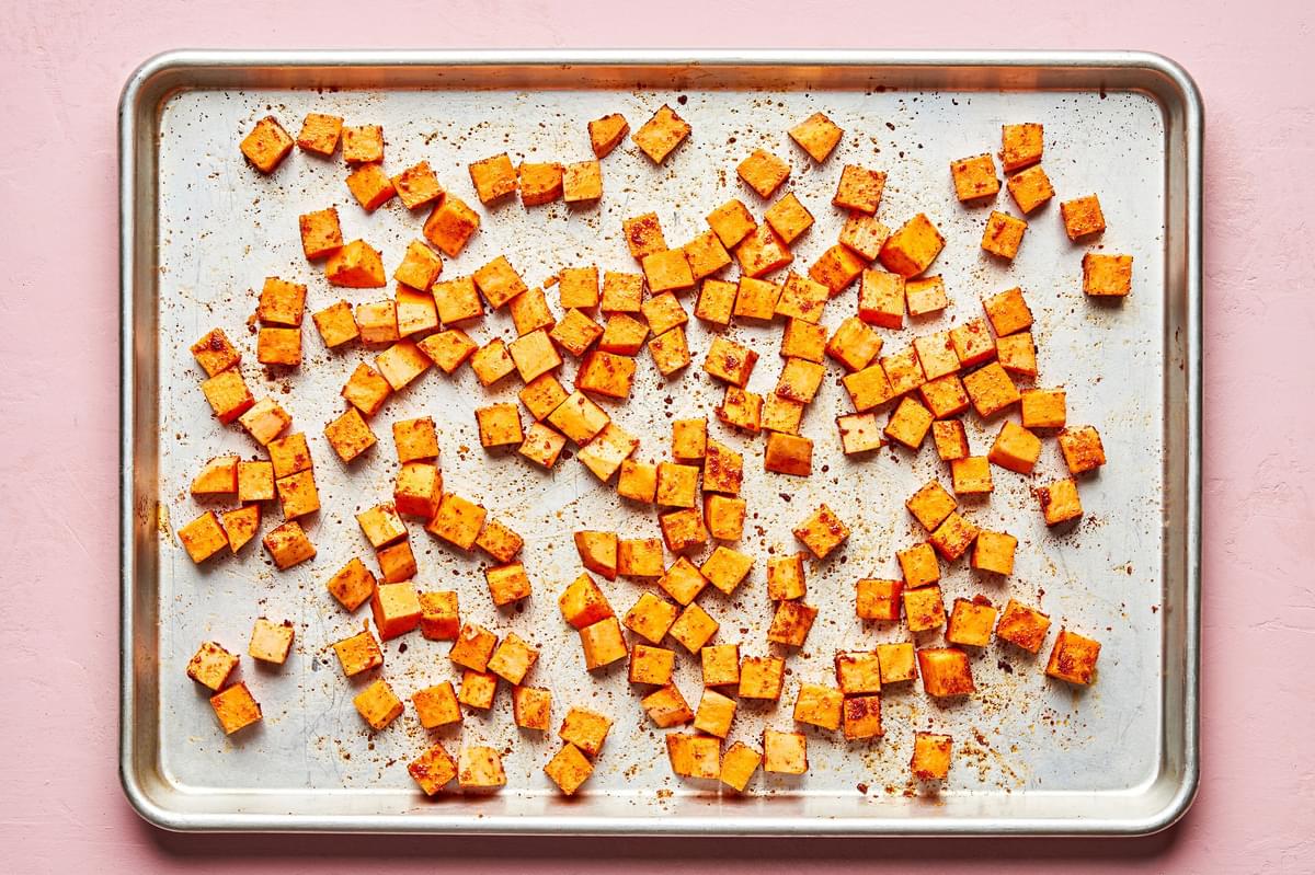 chopped sweet potatoes on a baking sheet tossed with olive oil paprika, chili powder, garlic powder, sugar and salt