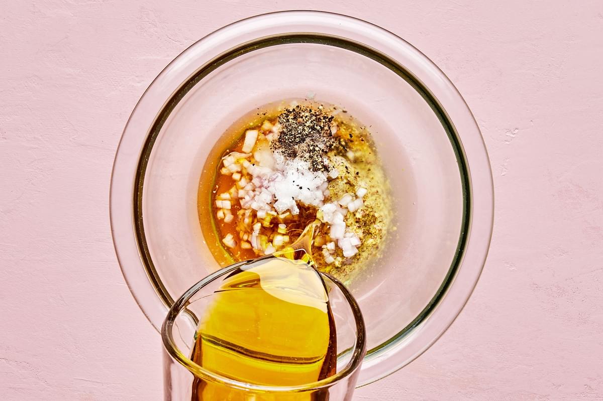 olive oil pouring into a bowl with stone ground mustard, honey, white wine vinegar, white balsamic, shallot, salt & pepper