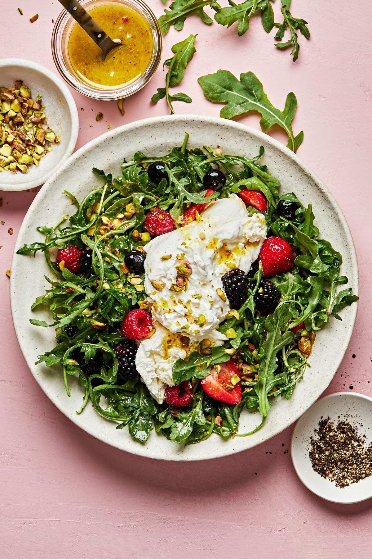 Burrata Salad with Summer Berries & Pistachios surrounded by bowls of pistachios, dressing and fresh cracked pepper