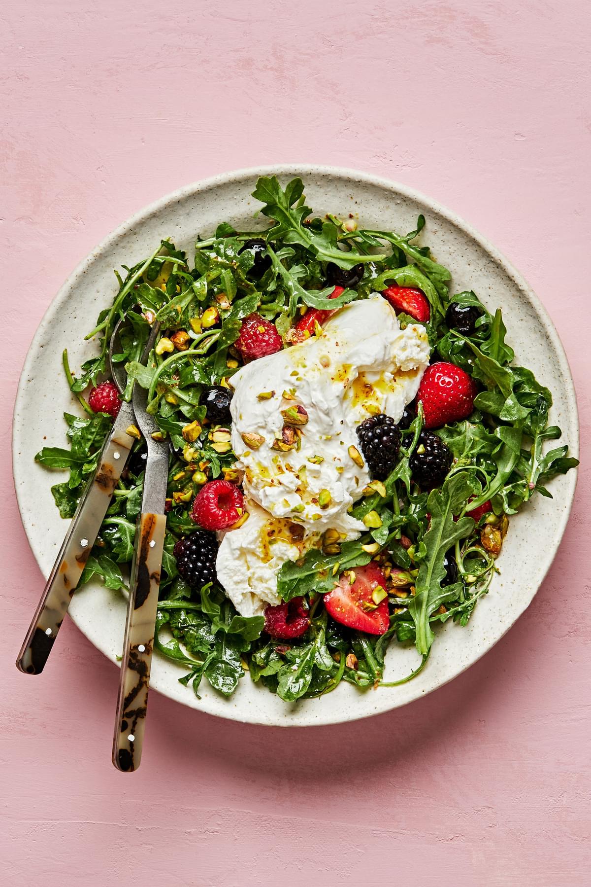 Burrata Salad with Summer Berries & Pistachios tossed with homemade balsamic vinaigrette in a serving bowl with salad servers