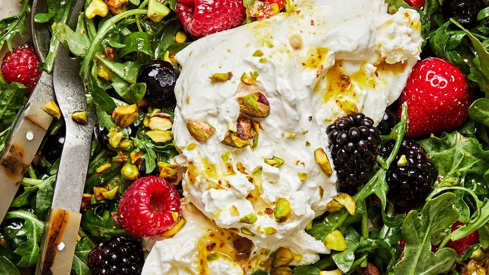 Burrata Salad with Summer Berries & Pistachios tossed with homemade balsamic vinaigrette in a serving bowl with salad servers