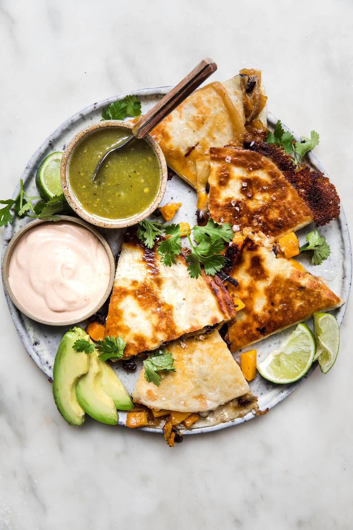 butternut squash quesadilla with caramelized onions on a plate served with avocado, salsa verde, chipotle cream & cilantro