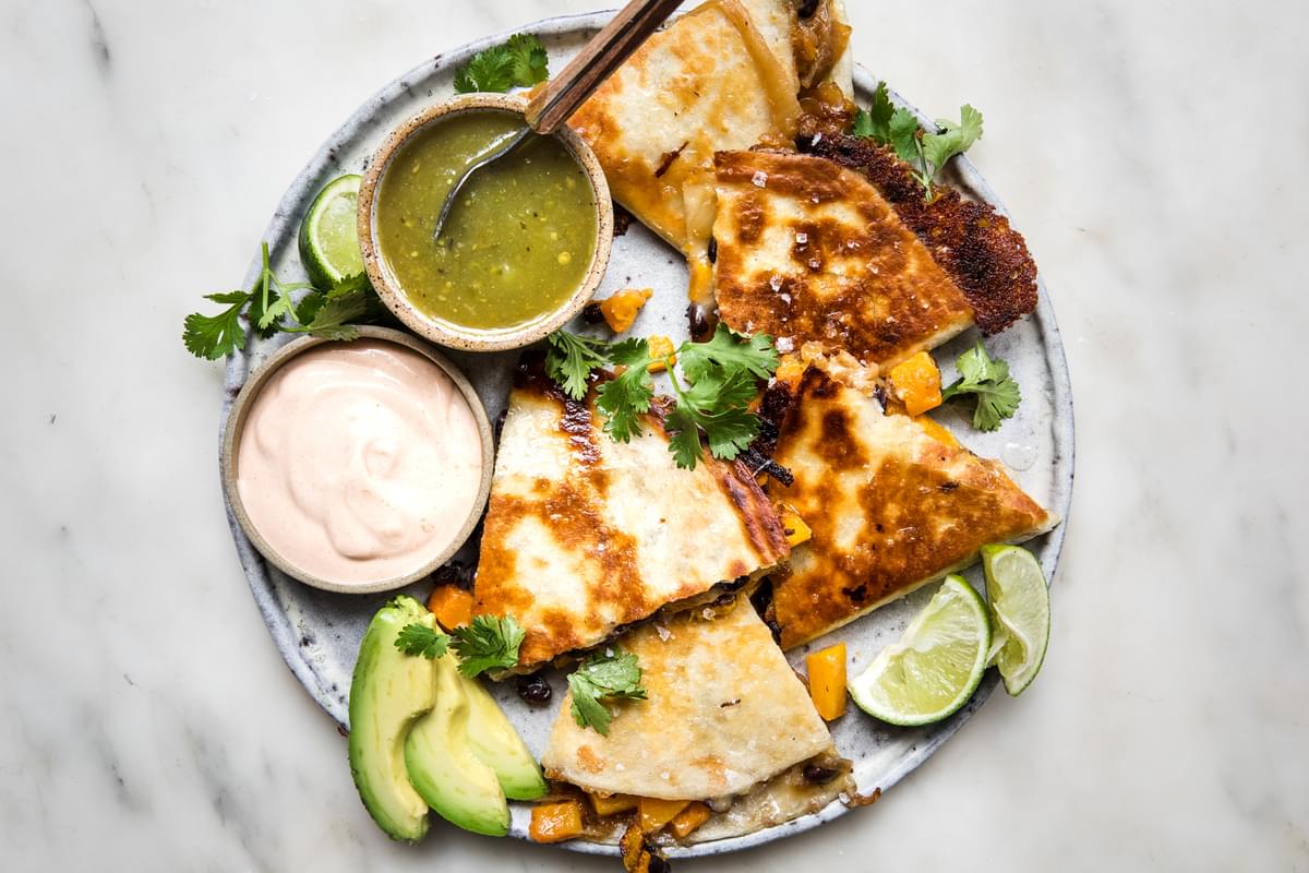 butternut squash quesadilla with caramelized onions on a plate served with avocado, salsa verde, chipotle cream & cilantro