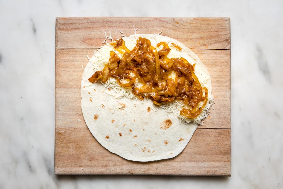 a flour tortilla with shredded mozzarella cheese and caramelized onions on half of it