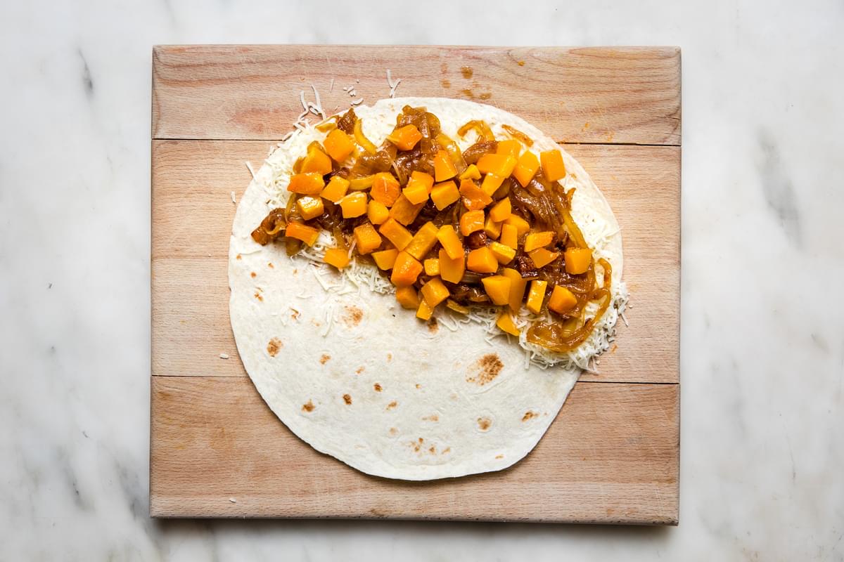 a flour tortilla with shredded mozzarella cheese, caramelized onions and roasted butternut squash on half of it