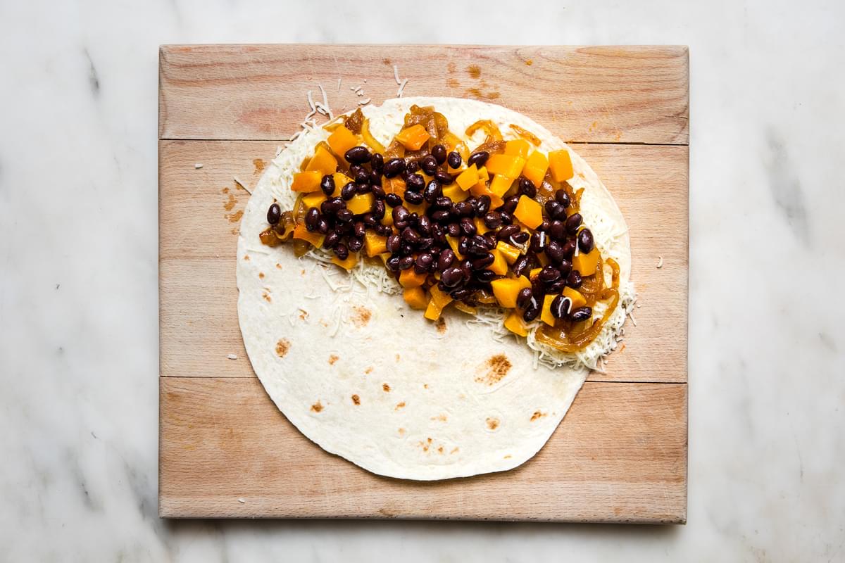 a flour tortilla with shredded mozzarella cheese, caramelized onions and roasted butternut squash & black beans on half of it