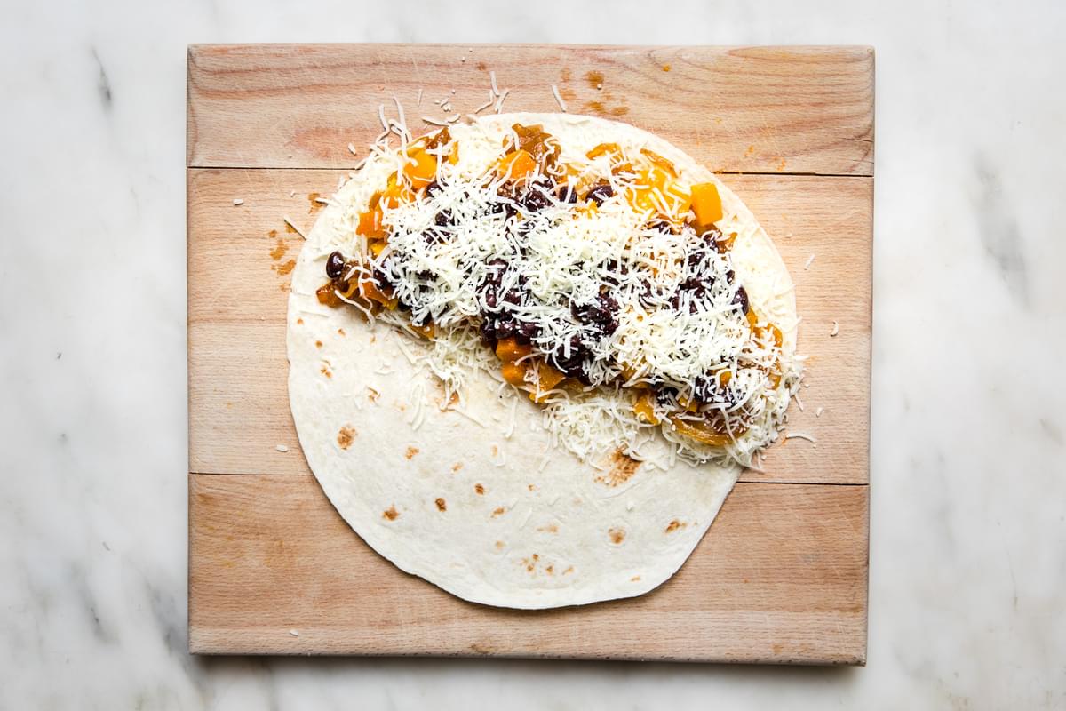 a flour tortilla with mozzarella, caramelized onions, roasted butternut squash & black beans on half of it