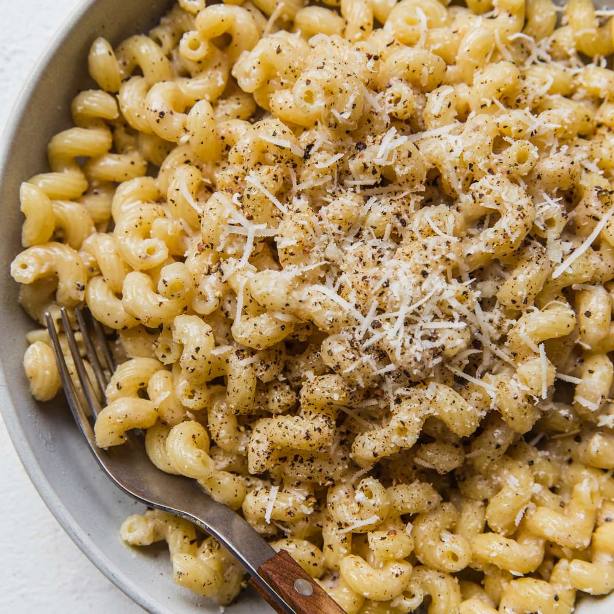 homemade Creamy Cavatappi in a bowl with a fork topped with grated Romano and coarsely cracked pepper