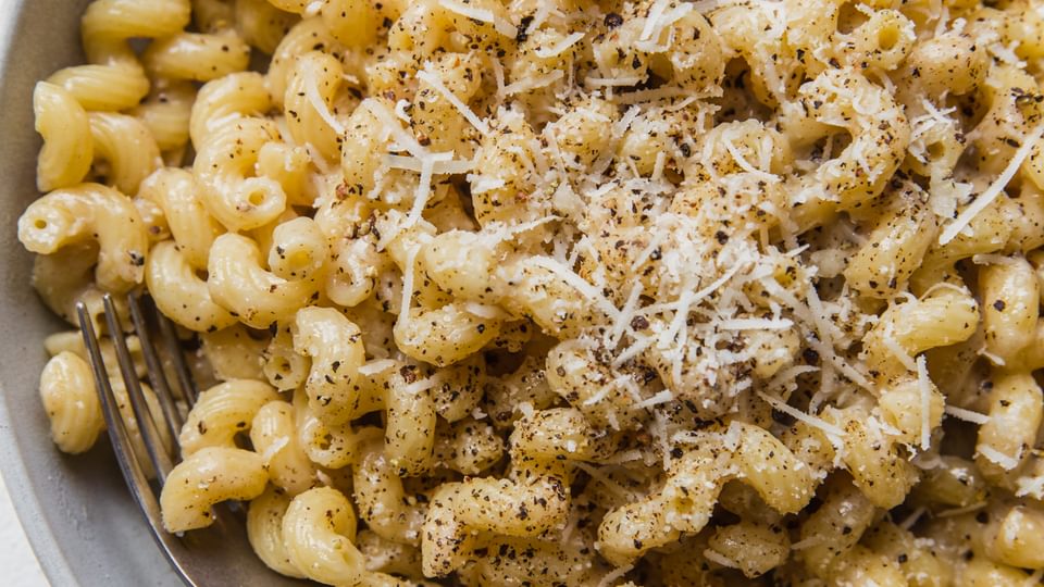 homemade Creamy Cavatappi in a bowl with a fork topped with grated Romano and coarsely cracked pepper