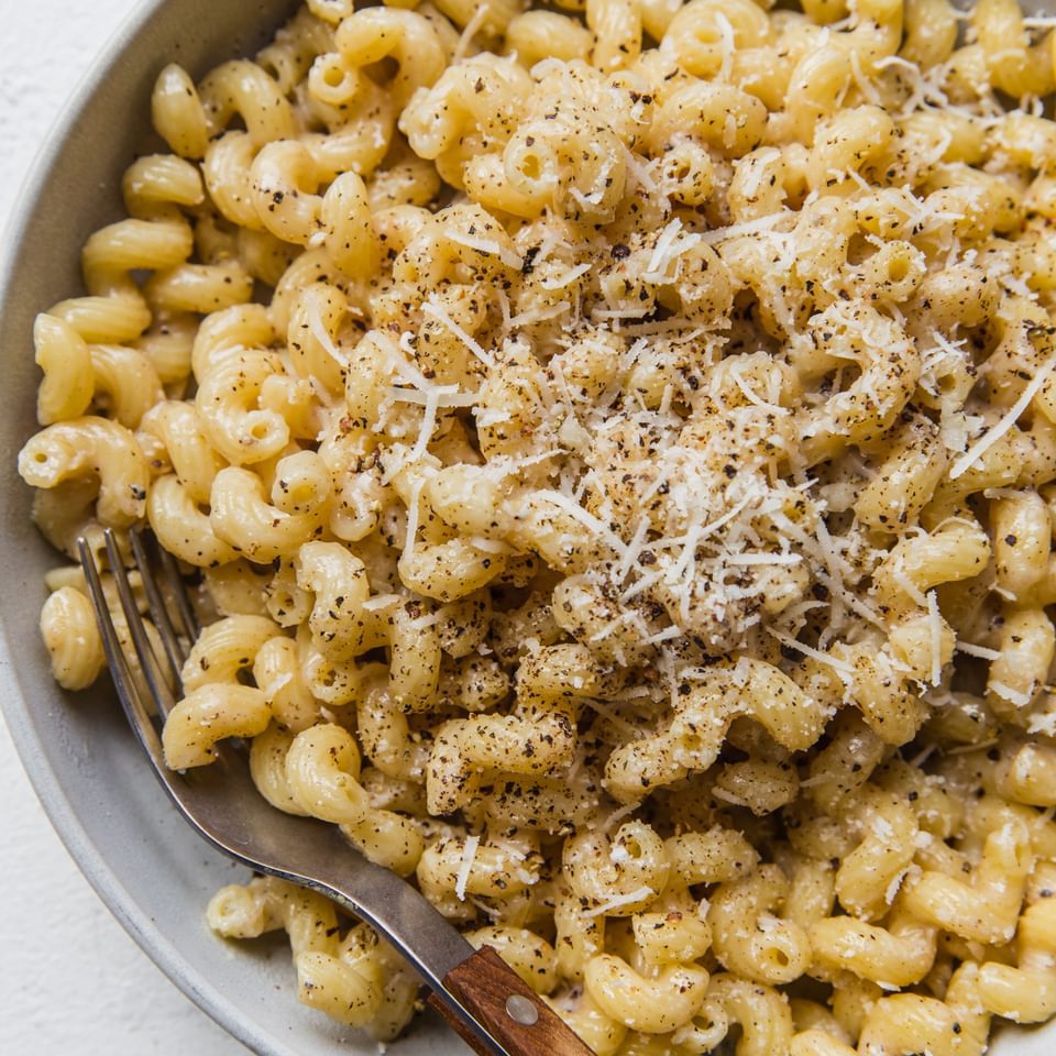 homemade Creamy Cavatappi Cacio e Pepe in a bowl with a fork topped with grated Romano and coarsely cracked pepper