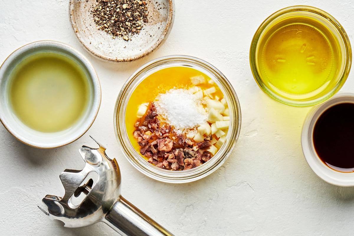 egg yolks, anchovies, garlic, lemon juice & salt in a jar next to bowls of olive oil, Worcestershire, lemon juice & pepper