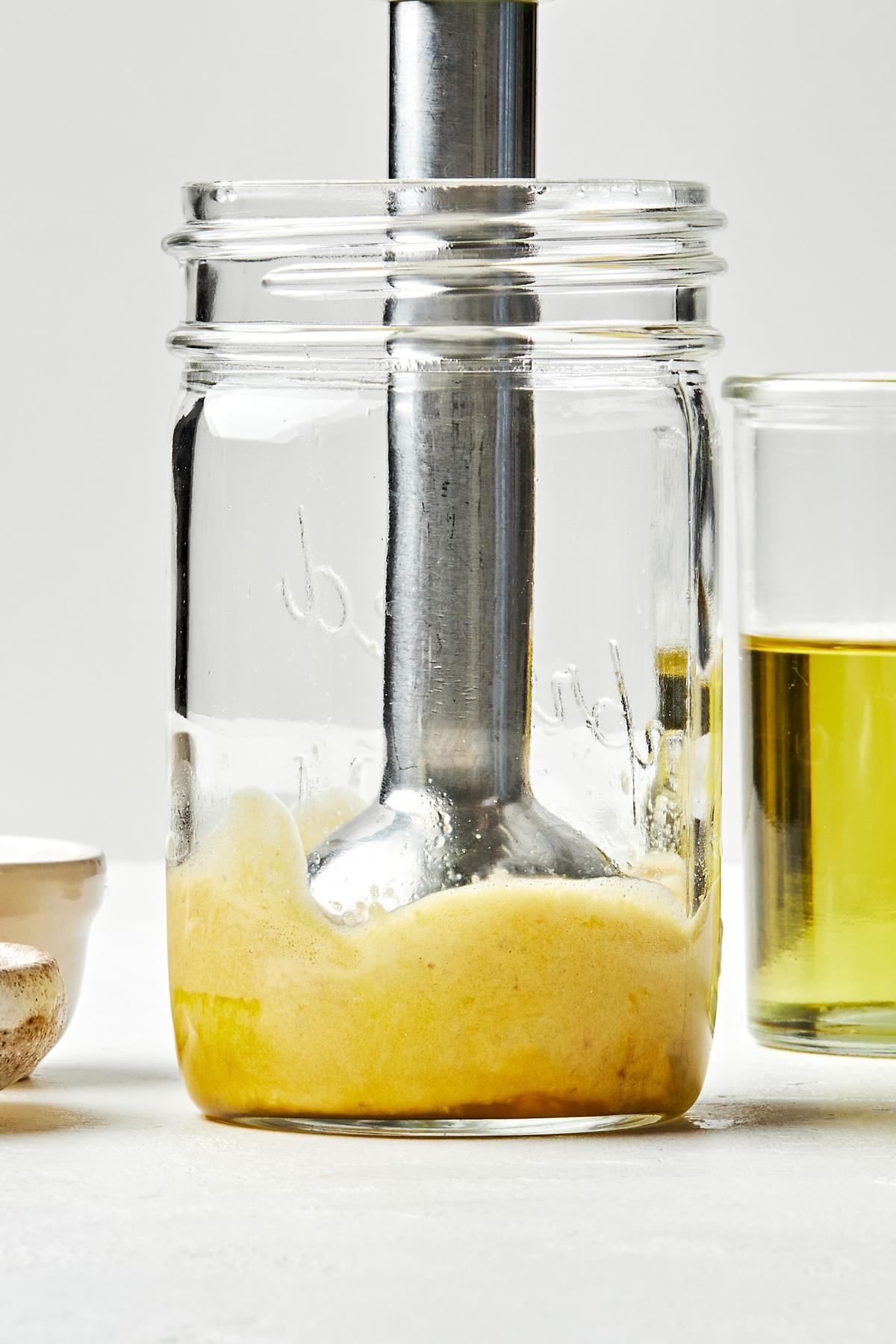 egg yolks, anchovies, garlic, lemon juice & salt being blended together in a glass jar with an immersion blender