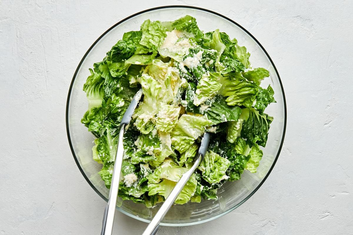 chopped romaine in a salad bowl being tossed with homemade Caesar dressing and finely grated parmesan