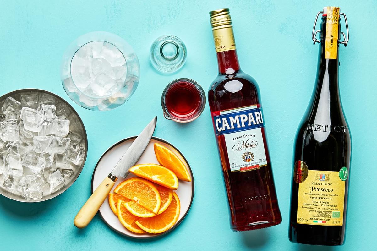 campari, prosecco, sparkling water, ice and orange wedges on the counter to make a campari spritz