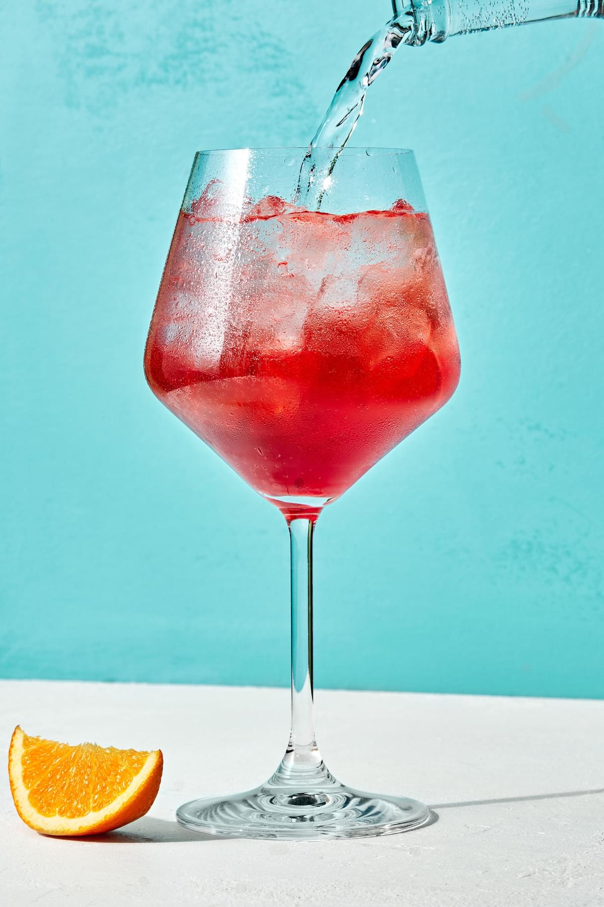 Sparkling water being poured into a wine glass with ice, prosecco and campari to make a campari spritz