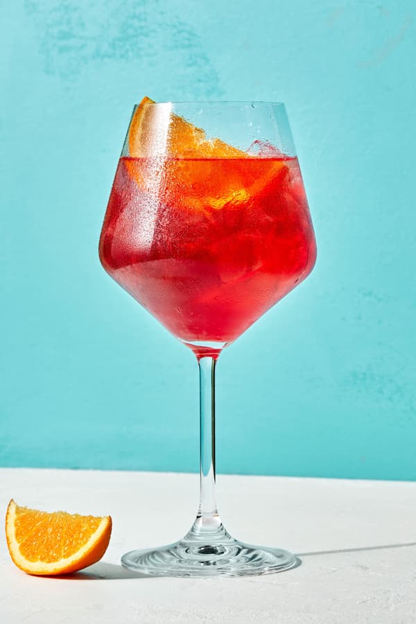 A campari spritz made with prosecco, Campari, sparkling water with an orange wedge for garnish