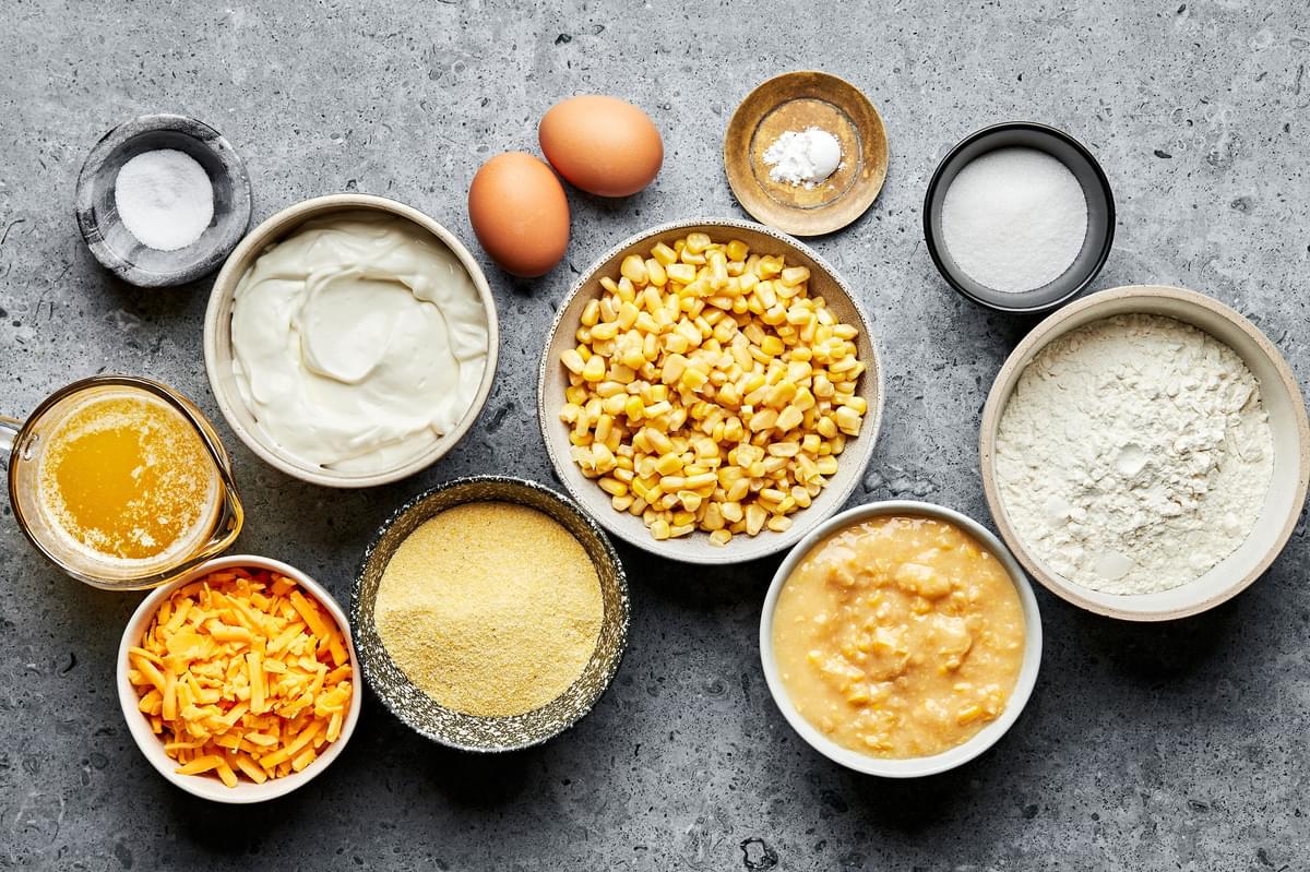 flour, cornmeal, sugar ,salt, baking powder, butter, eggs, creamed corn, corn, sour cream and  cheese in bowls on the counter