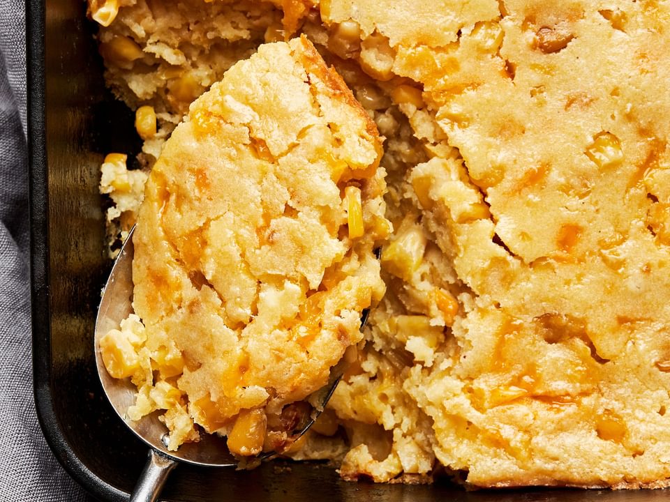 cheesy corn casserole made with corn and creamed corn in a casserole dish with a spoon scooping out a serving