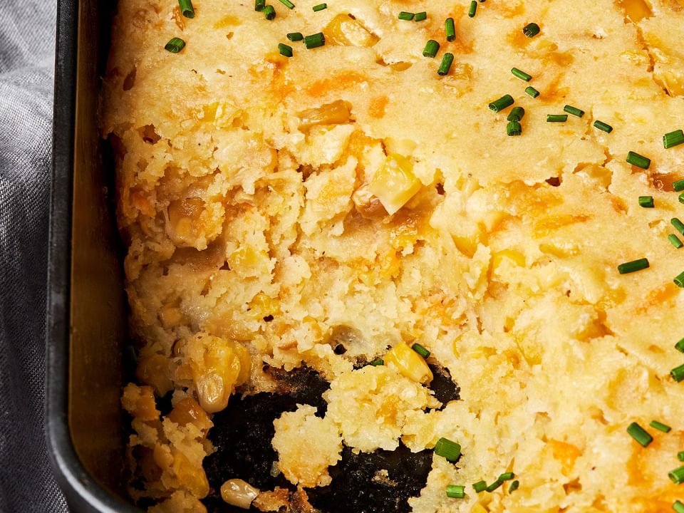 cheesy corn casserole made with butter, flour, cornmeal, sour cream and eggs  in a casserole dish with a scoop taken out