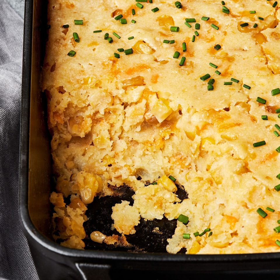 cheesy corn casserole made with butter, flour, cornmeal, sour cream and eggs  in a casserole dish with a scoop taken out