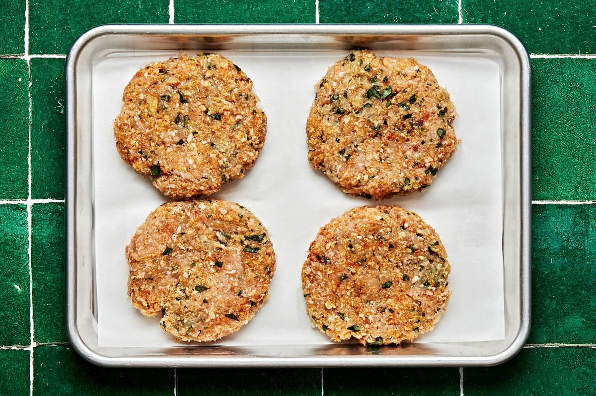 chicken burger patties on a parchment lined baking sheet made with ground chicken, breadcrumbs, basil, parmesan and spices
