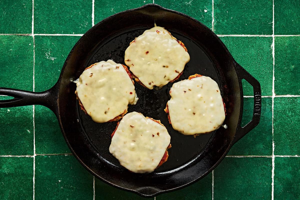 homemade chick burger patties being fried in a skillet with pepper jack cheese slices melting on top