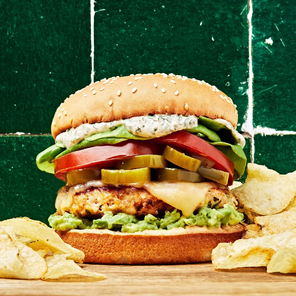 chicken burger with basil mayo, avocado spread, candied jalapeños, pepper jack cheese, lettuce and tomato on a cutting board